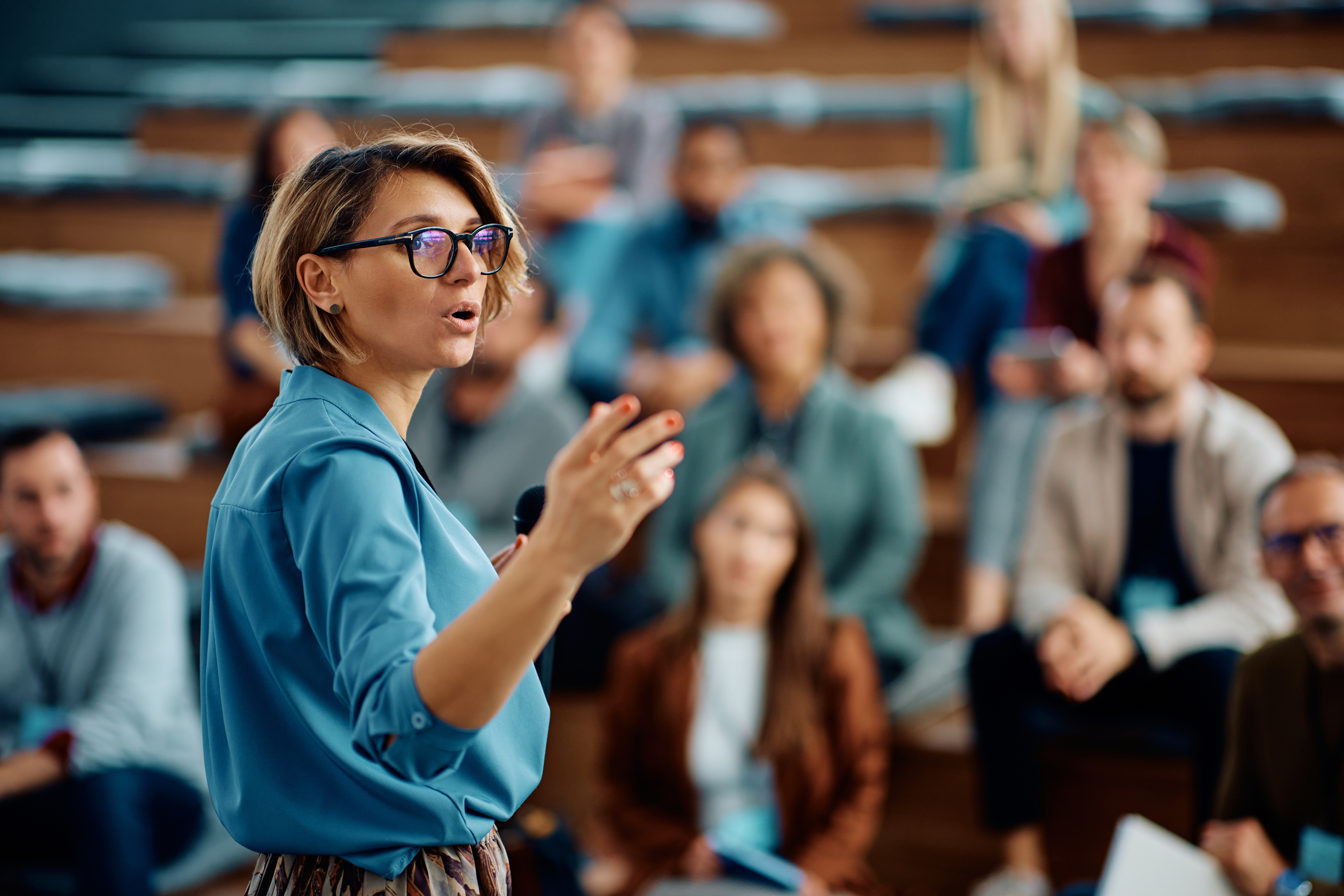 A woman with short hair and glasses presenting in front of a crowd.